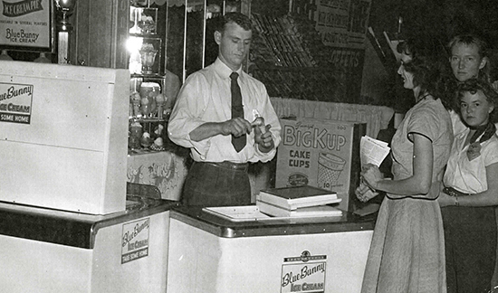 Old time photo of a man scooping ice cream at a parlor